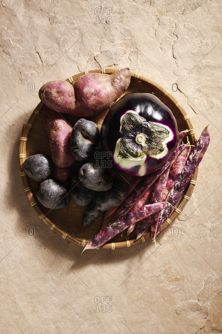 Sweet potatoes, black potatoes, a round aubergine and borlotti beans in a woven bamboo basket
