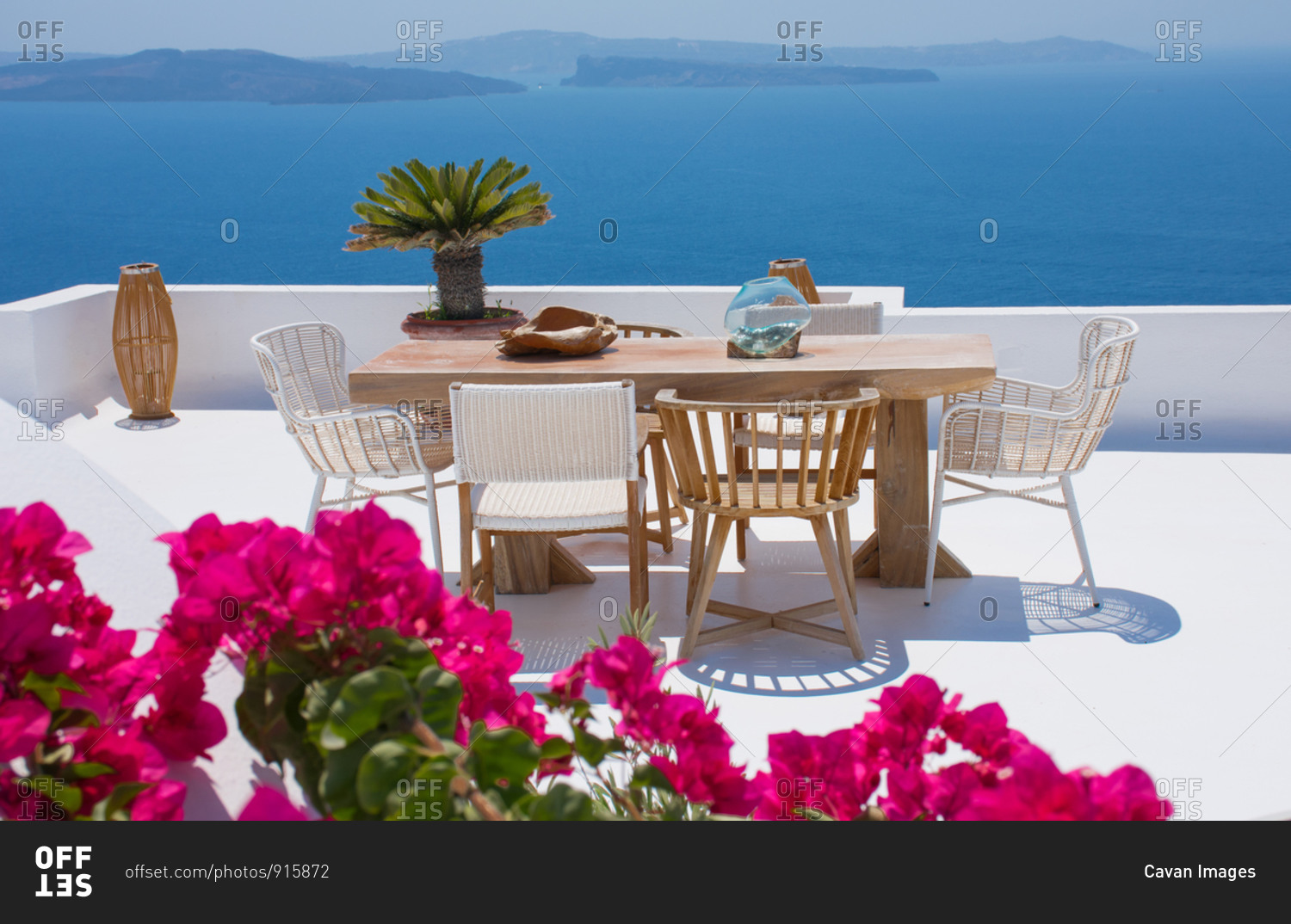 furniture composed by a table and some chairs on a white floral terrace of a house in Santorini Greece where you can enjoy a meal while seeing a romantic seascape to the blue Aegean sea. Hori