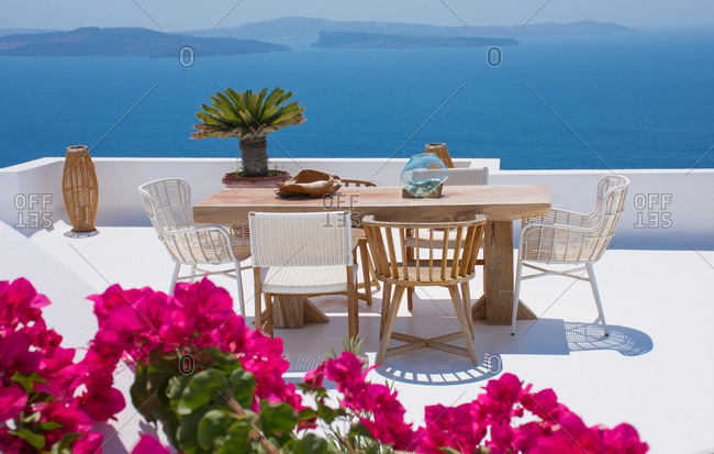 furniture composed by a table and some chairs on a white floral terrace of a house in Santorini Greece where you can enjoy a meal while seeing a romantic seascape to the blue Aegean sea. Hori