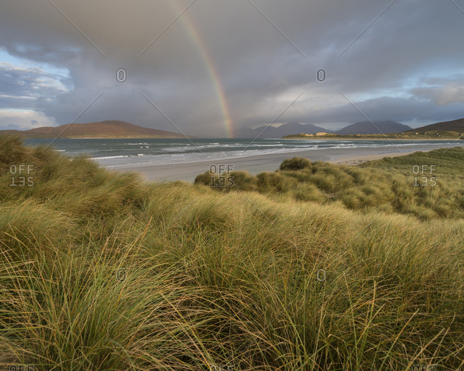 Rainbow shines above sea and coastal sand dunes at Seilebost beach, Isle of Harris, Scotland