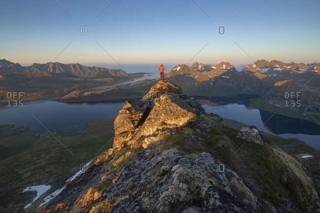 Male hiker overlooks mountain landscape of Selfjord area from summit of Kitind, Moskenes√∏y, Lofoten Islands, Norway