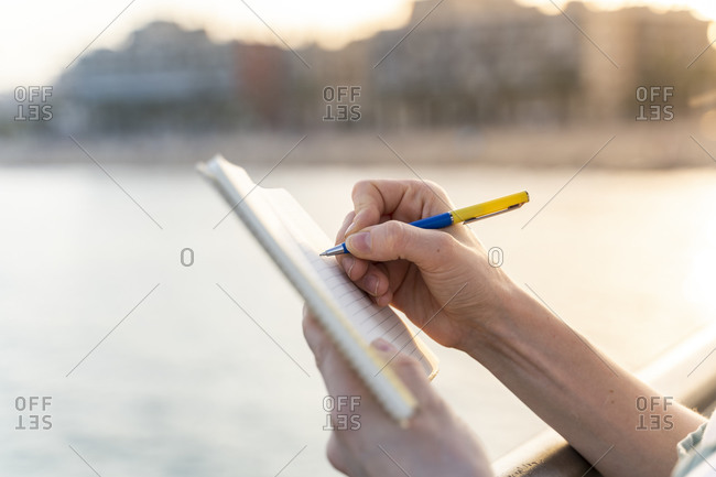 Crop view of young woman writing in notebook at evening twilight