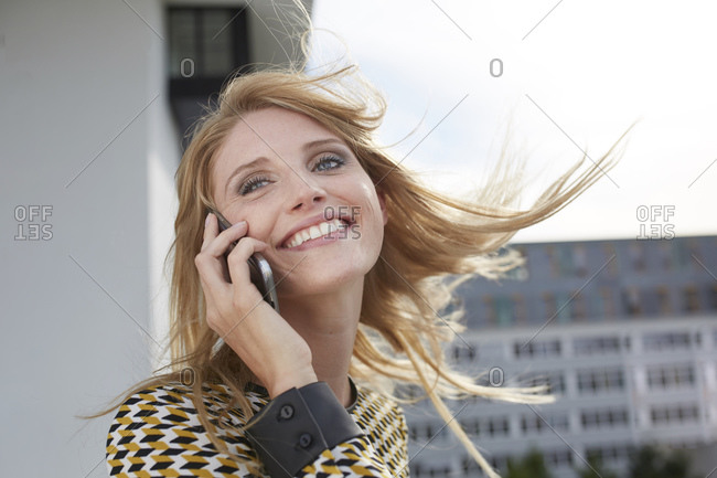 Portrait of happy blond young woman with windblown hair on the phone
