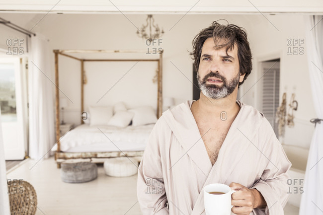 Man wearing bathrobe with a cup of coffee in bedroom