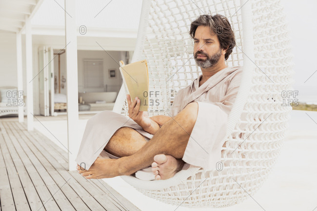Relaxed man in bathrobe reading a book in hanging chair