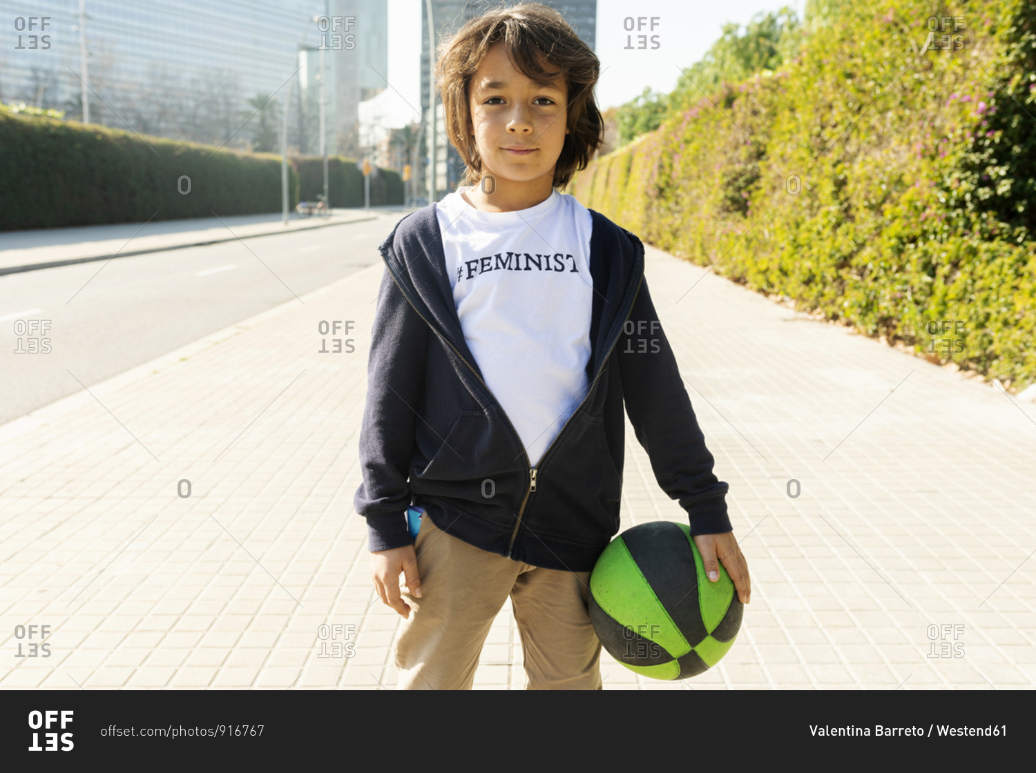 Little boy standing in the street with print on t-shirt- saying Feminist- holding ball