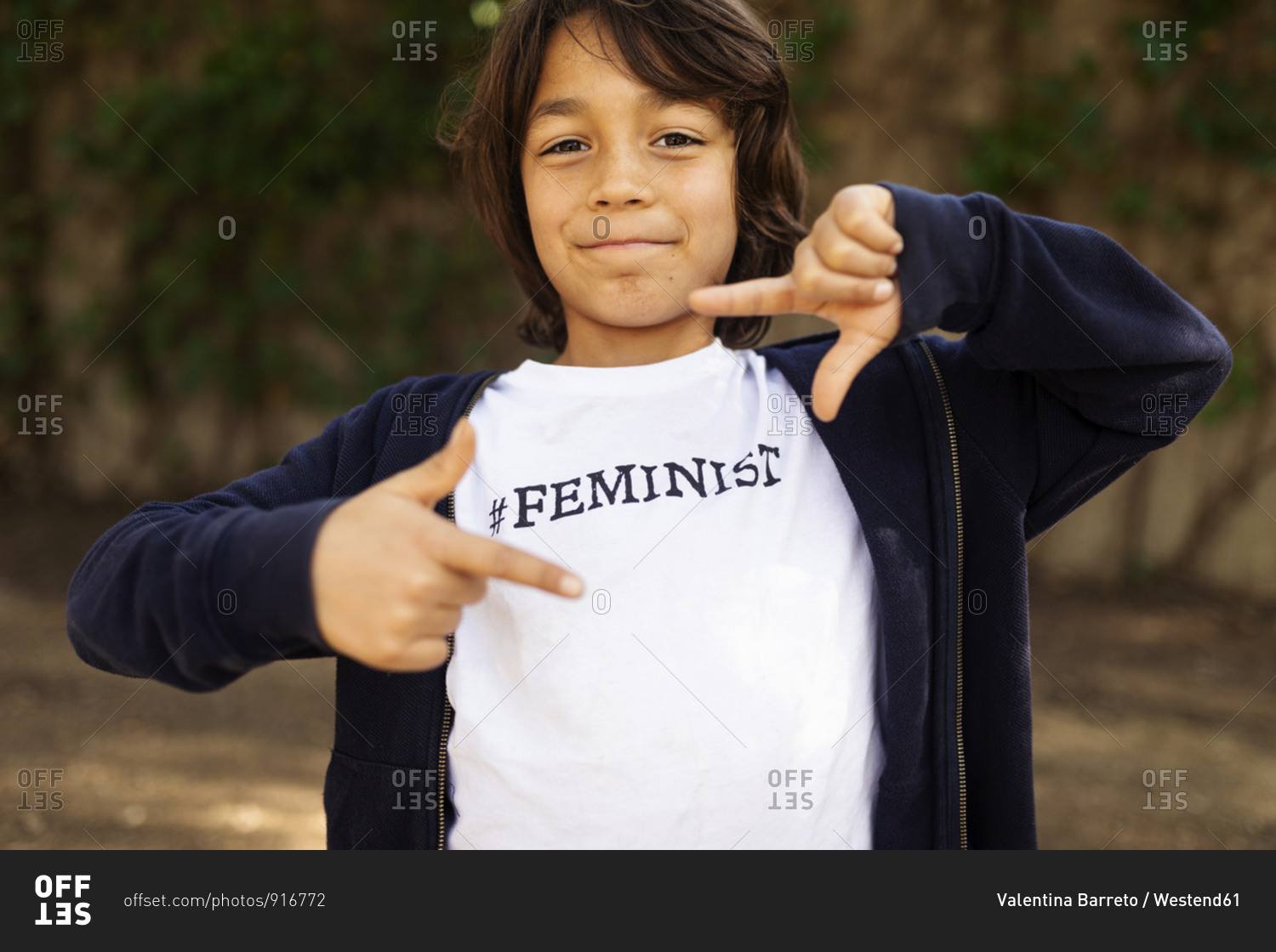 Little boy standing in the street with print on t-shirt- saying Feminist- making finger frame