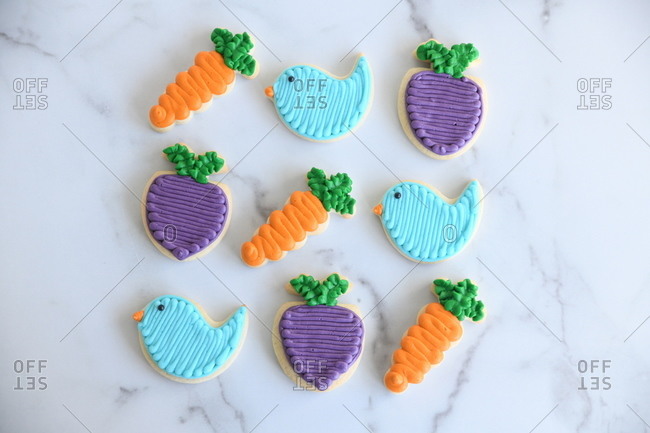 Overhead view of colorful bird, carrot and turnip Easter cookies on marble surface