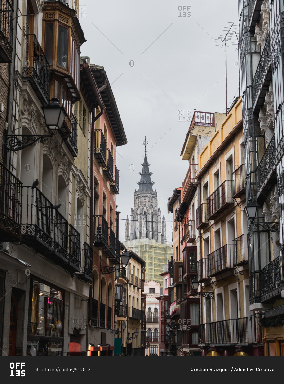 From below of narrow street of city Toledo in Spain with old residential buildings and cathedral in background against gray cloudy sky