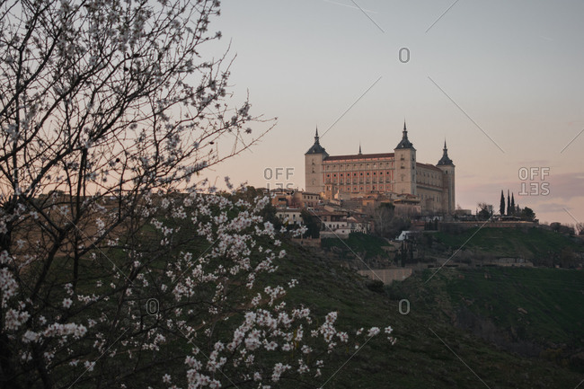 Beautiful medieval castle on hill with frame of blooming tree against sunset sky in spring evening in province of Toledo in Spain