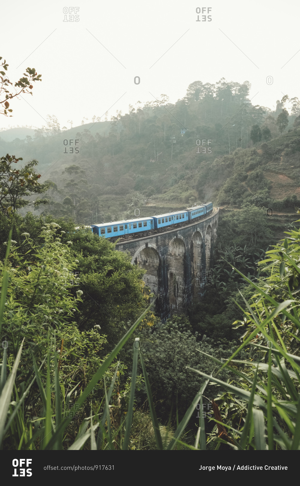 From above of blue train on stone bridge among tropical green jungles in foggy weather in Sri Lanka Asia