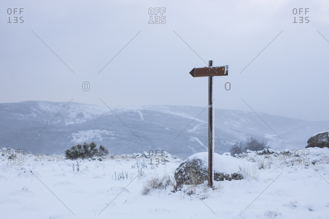Small wooden guide sign on rocky roadside with mountainous terrain and blue cloudy sky on background