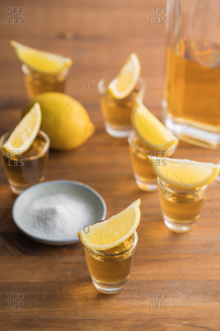 From above glass shots of golden tequila with salty rim and slices of lemon on top on wooden table