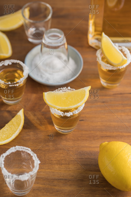From above top view of glass shots of golden tequila with salty rim and slices of lemon on top on wooden table