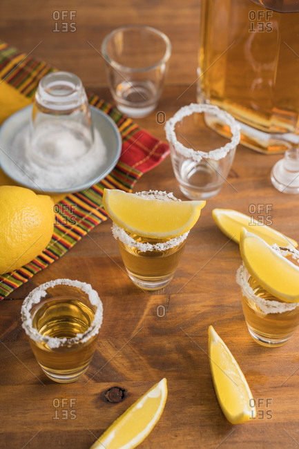 From above top view of glass shots of golden tequila with salty rim and slices of lemon on top on wooden table