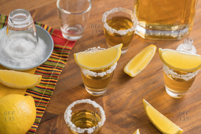 From above top view of glass shots of golden tequila with salty rim and slices of lemon on top on wooden table