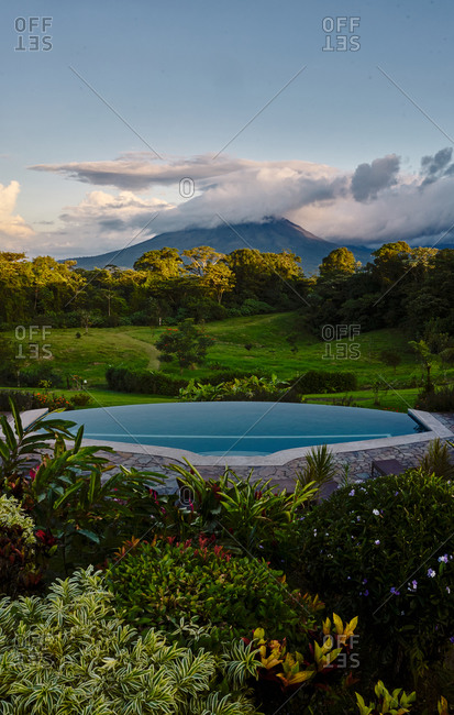 Swimming pool with clean water located near exotic plants in green valley near mountain peak in cloudy evening in Costa Rica