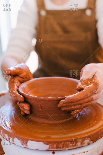 High angle of crop person in casual clothes making handmade pottery using special equipment while working in light contemporary studio