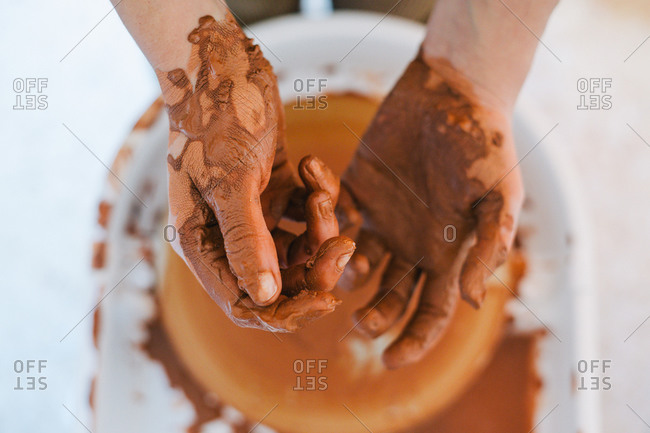 From above of crop person hands in brown clay after making pottery against blurred special equipment in light modern workshop