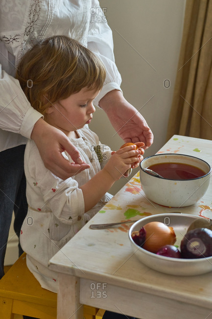 Little girl dyeing eggs for Easter at home with her mother. Indoor spring activities. Natural dyes made from organic vegetables and spices