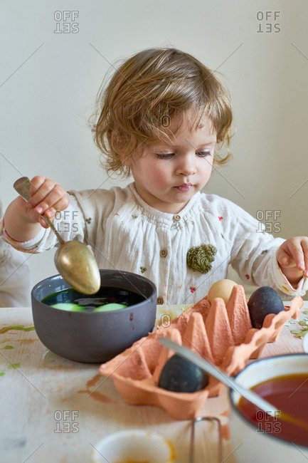 Little girl painting eggs for Easter at home with her mother. Indoor spring activities. Natural dyes made from organic vegetables and spices