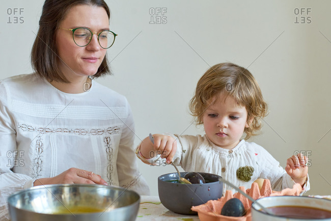 Little girl dyeing eggs for Easter at home with her mother. Indoor spring activities. Natural dyes made from organic vegetables and spices