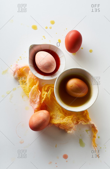 Top view image of colorful painted eggs in small white bowls on neutral background with negative space