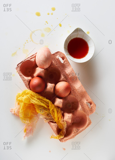 Top view image of colorful painted eggs, bowl with dyeing liquid and egg carton on neutral background with negative space