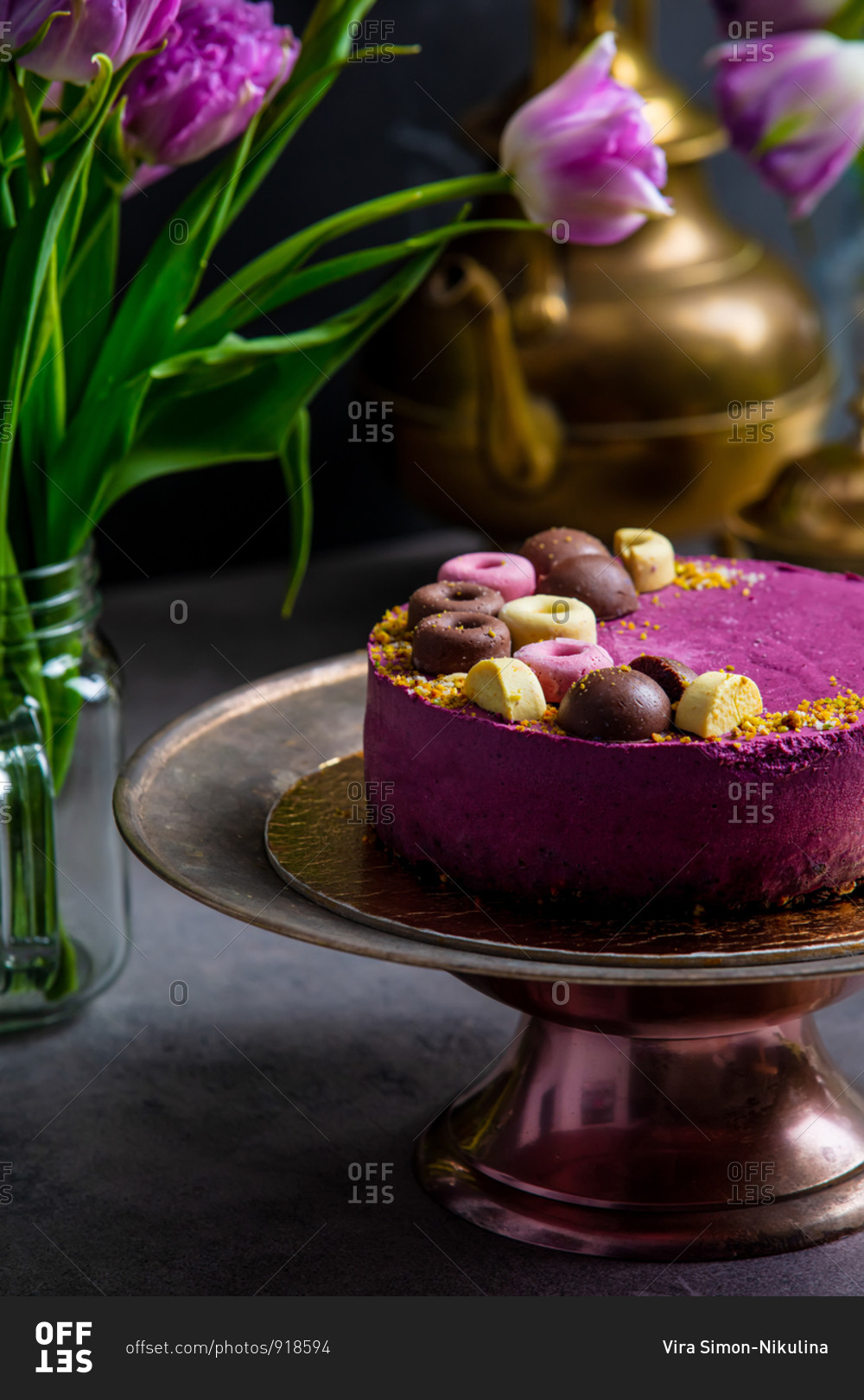 Raw cake made of black currant, cashew, coconut oil and cocoa on a stand surrounded by tulips