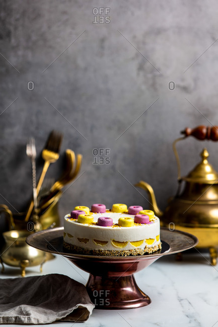 Raw cake made of mango, cashew, coconut oil , blueberries, dates on a stand surrounded by kitchenware