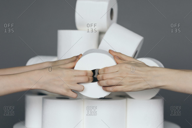 Two hands pulling on a roll of toilet paper with more toilet paper in the background