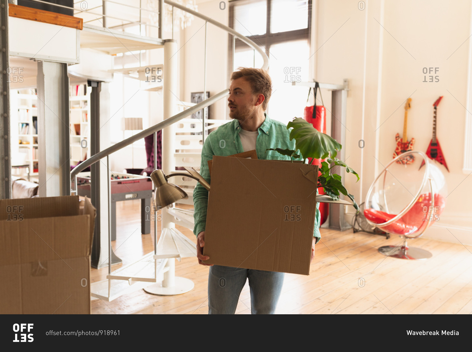 Front view of a young Caucasian man wearing green shirt, moving in to a new apartment, holding a cardboard box