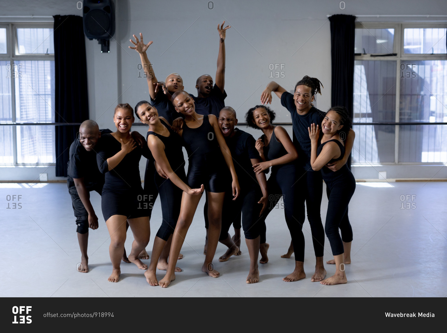Front view of a multi-ethnic group of fit male and female modern dancers wearing black outfits practicing a dance routine during a dance class in a bright studio, standing together, smiling and looking straight into a camera.