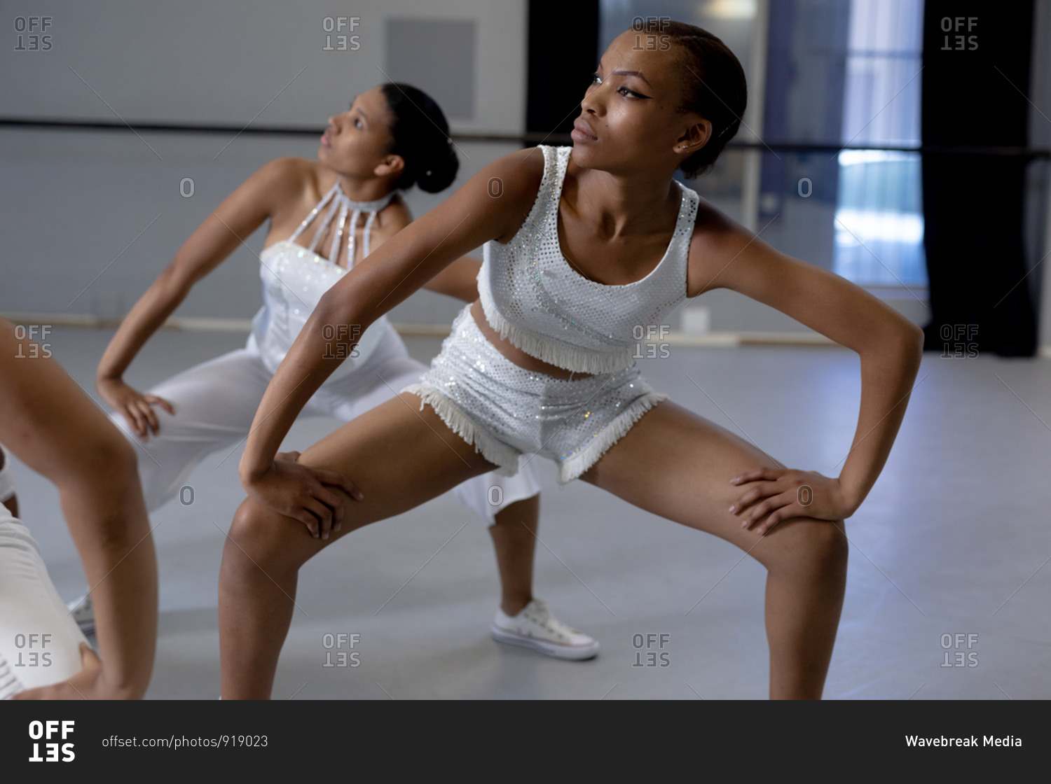 Front view close up of two mixed race fit female modern dancers wearing white outfits practicing a dance routine during a dance class in a bright studio.
