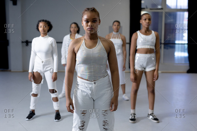 Multi-ethnic group of fit female modern dancers wearing white outfits practicing a dance routine during a dance class in a bright studio while looking straight into camera