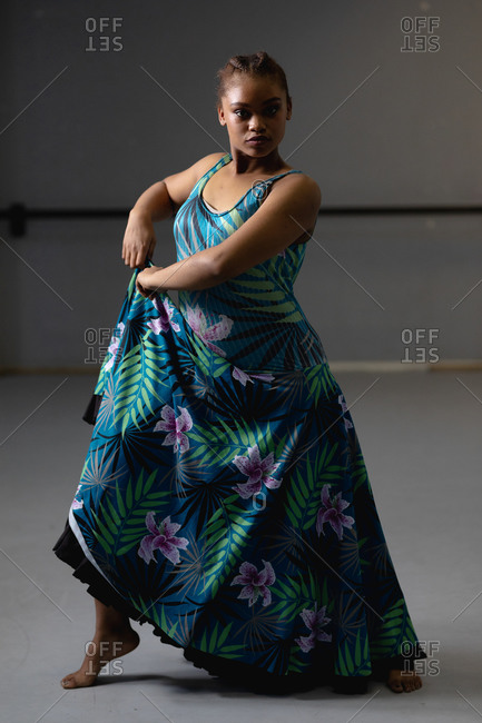 Portrait of a mixed race female dancer wearing blue floral dress, holding a fold and looking straight into a camera.
