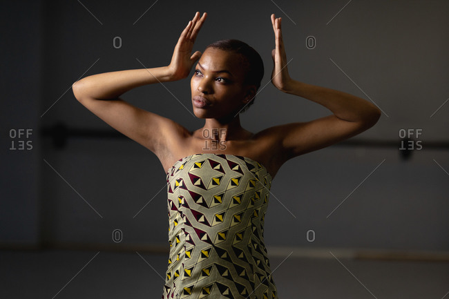 Front view close up of a mixed race female dancer wearing yellow dress, dancing in a studio with her hands up.
