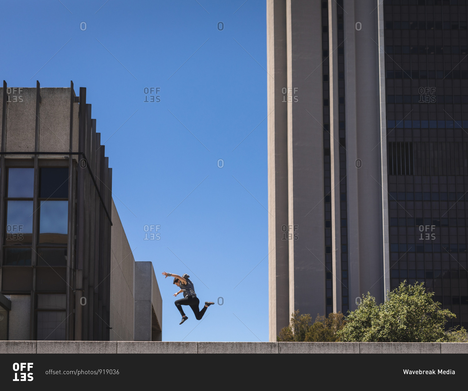 Side view of a Caucasian man practicing parkour by the building in a city on a sunny day, jumping up between modern buildings.