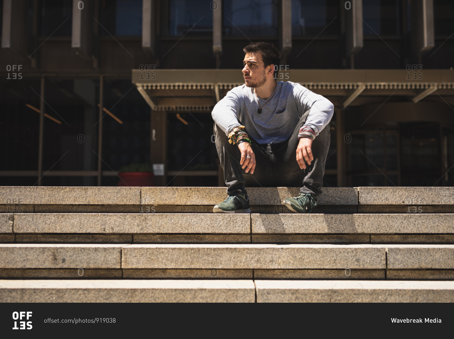 Front view of a Caucasian man practicing parkour by the building in a city on a sunny day, resting taking a break, sitting on the stairs.