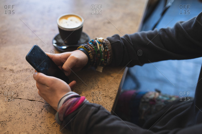 Side view mid section of a Caucasian man wearing casual clothes, sitting by a table in a coffee shop, using his smartphone, with a cup of coffee standing on a table.
