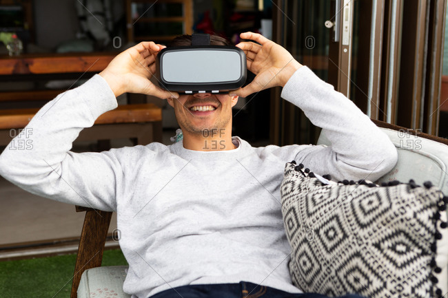 Front view close up of a Caucasian man hanging out on a balcony on a sunny day, wearing VR goggles and smiling