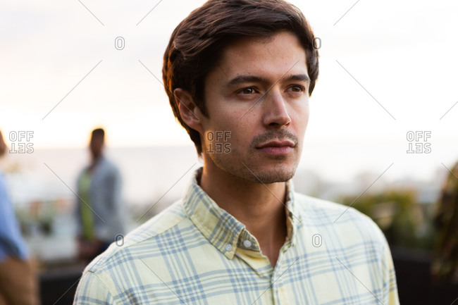 Front view close up of a Caucasian man hanging out on a roof terrace on a sunny day, looking away from camera