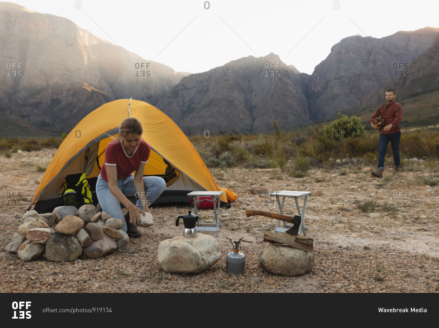 Side view of a Caucasian couple having a good time on a trip to the mountains, a woman is building a campfire, while a man is collecting