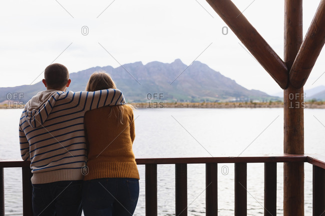 Rear view of a Caucasian couple having a good time on a trip to the mountains, standing on a balcony in a cabin, embracing, enjoying view