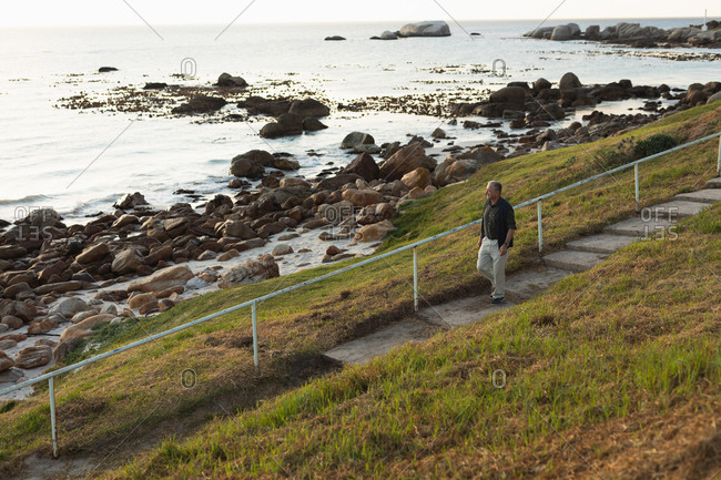 Side view of a senior Caucasian man walking down stairs in the countryside by the sea, admiring a coastal view
