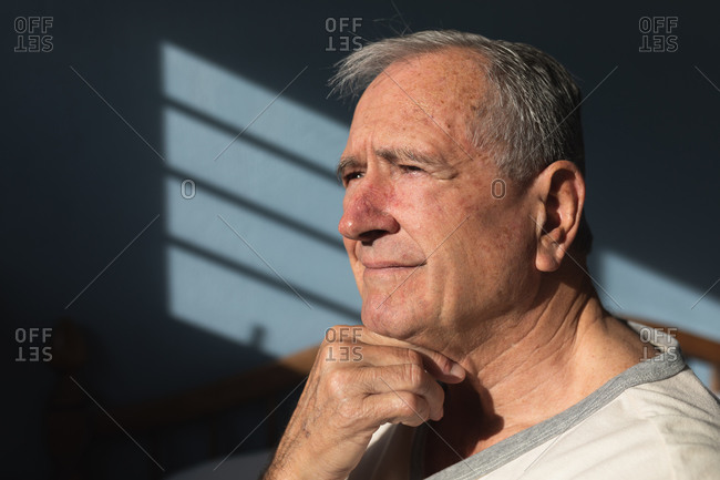 Side view close up of a senior Caucasian man relaxing at home in his bedroom, sitting in the sun and thinking, after getting up in the morning