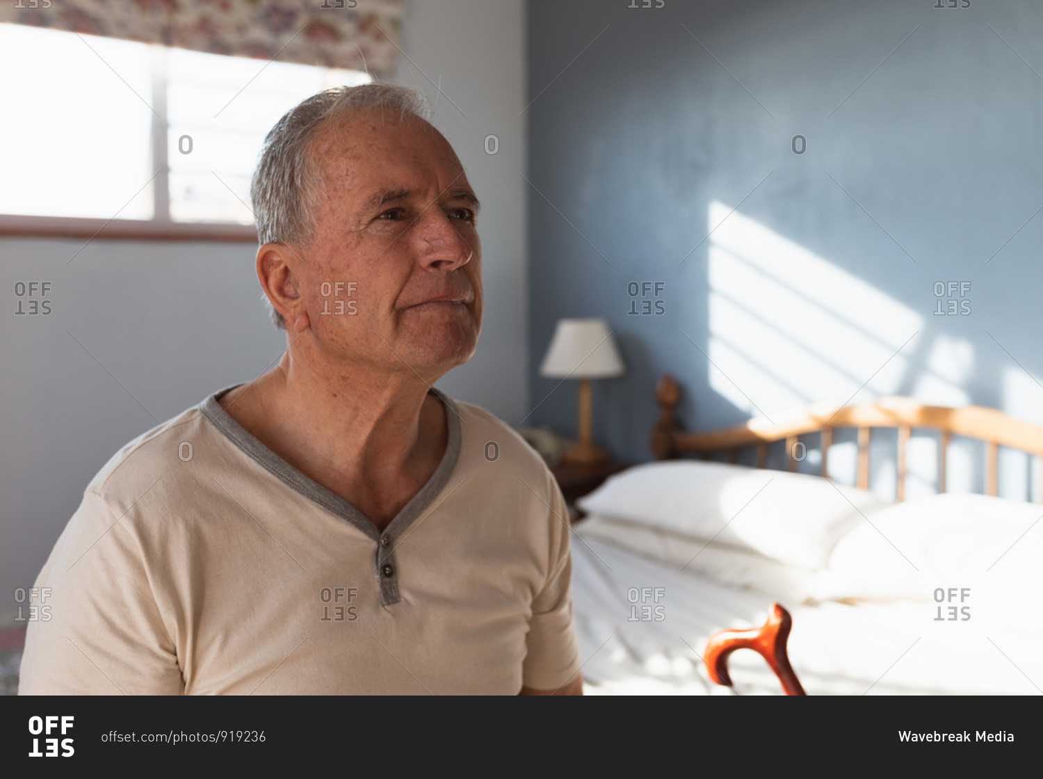 Side view close up of a senior Caucasian man relaxing at home in his bedroom, sitting on the side of his bed with his cane and thinking, after getting up in the morning