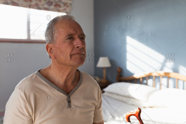 Side view close up of a senior Caucasian man relaxing at home in his bedroom, sitting on the side of his bed with his cane and thinking, after getting up in the morning