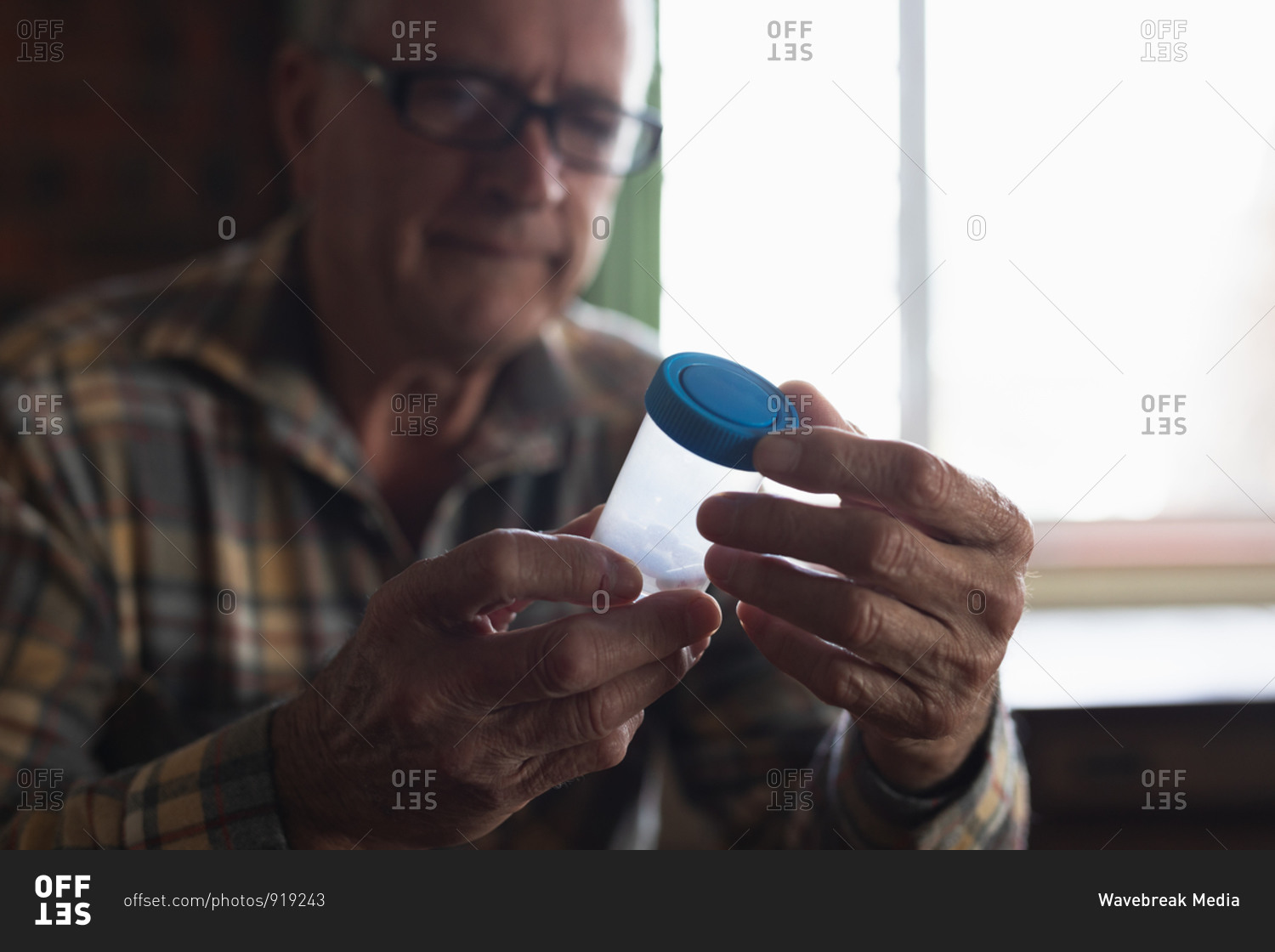 Front view close up of a senior Caucasian man sitting at home holding pill box of medication, focus on the foreground