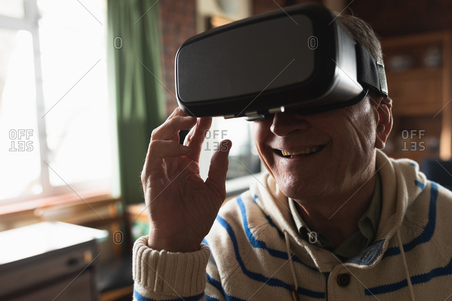 Side view close up of a senior Caucasian man relaxing at home in his living room, sitting at the table using a virtual reality headset